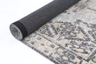 Alayah Ornamental Charcoal & Beige Rug rolled photos with dark backing on white flooring