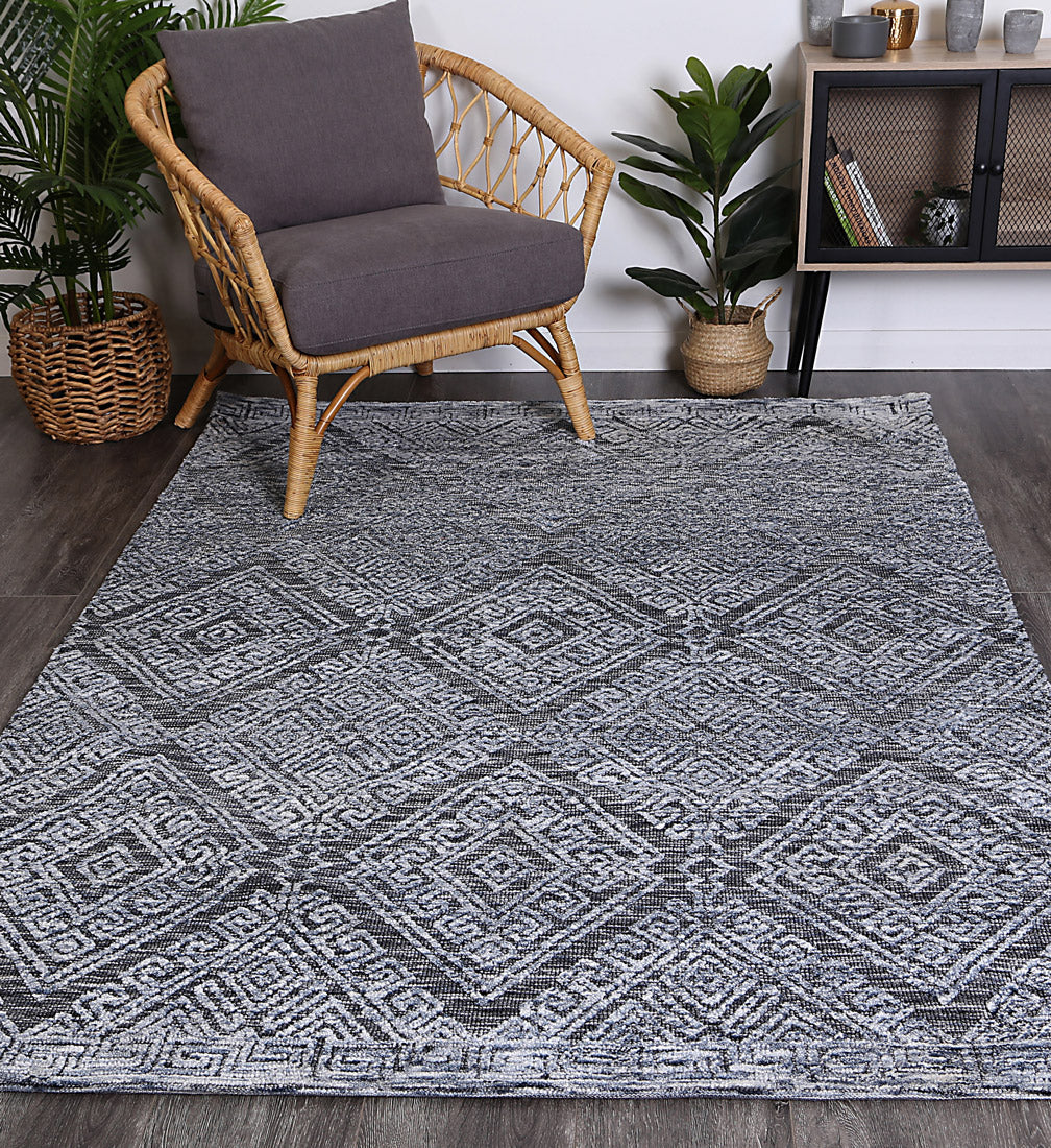 Alayah Diamond Blue Rug in living room on dark flooring with wicker chair