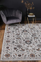 Almada Charcoal Floral Rug in lounge room with grey velvet chair on natural wood floors, with gold and brass accessories